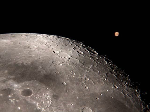 Sur cette image prise depuis la Terre par Wayman, Mars apparaît bien petite dans l'objectif du télescope. La présence de la Lune permet de se rendre compte de la difficulté de l'observation des surfaces planétaires à cette distance.